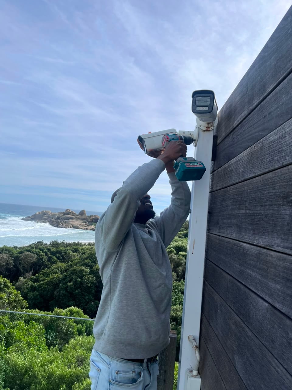 One of our technicians fitting a bullet camera to a pole on a coastal Cape Town property, the Atlantic behind him.