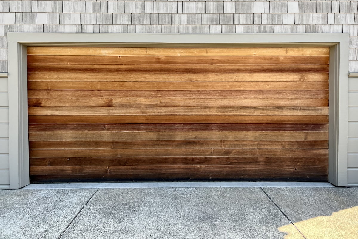 A timber-clad sectional garage door, part way open on its rail.