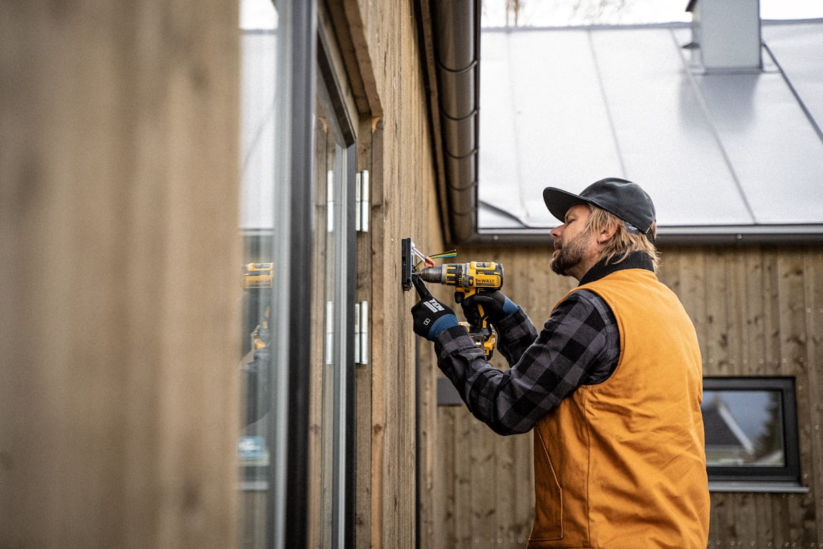 An installer drilling a fixing into an exterior wall with a cordless drill.